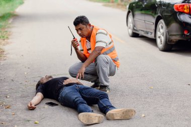 Acil yardım ekipleri telsizini çalarken yolda baygın bir şekilde yatan bir adam.