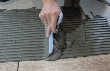 Erkek eli yere seramik fayanslar döşemek için çimento harcı uygular..