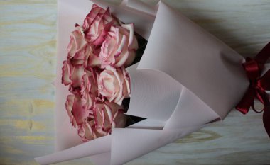 Güzel bir buket pembe gül, açık ahşap bir yüzeyde yatıyor..