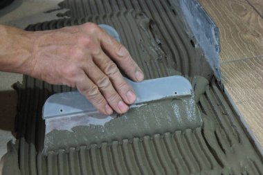 İşçinin eli seramik fayanslar için çimento harcı olarak spatula kullanıyor..