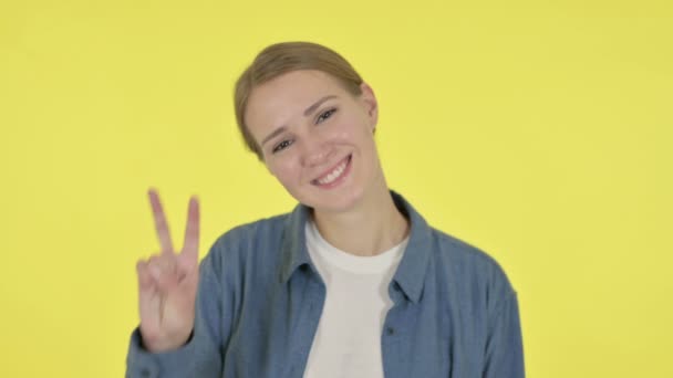 Mujer joven mostrando signo de victoria sobre fondo amarillo — Vídeos de Stock