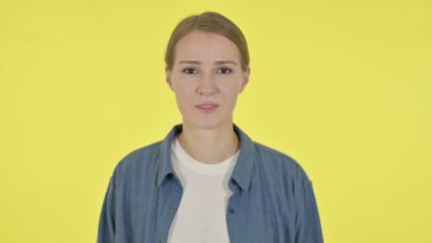 Seriös ung kvinna tittar på kameran på gul bakgrund — Stockvideo