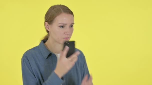 Jovem mulher falando irritado no telefone no fundo amarelo — Vídeo de Stock