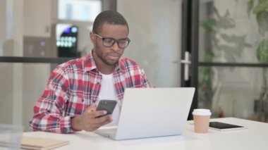 Laptop kullanırken Akıllı Telefon kullanan Afrikalı Adam 