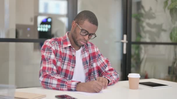 African Man Γράφοντας σε χαρτί στο γραφείο — Αρχείο Βίντεο