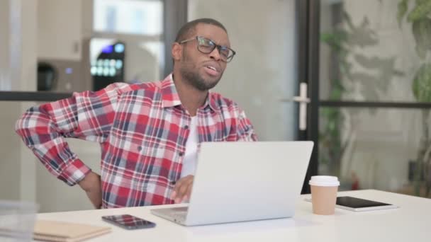 Hombre africano que tiene dolor de espalda mientras usa el ordenador portátil — Vídeos de Stock