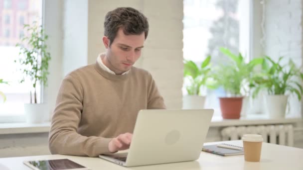 Чоловік дивиться на камеру, користуючись ноутбуком у офісі — стокове відео