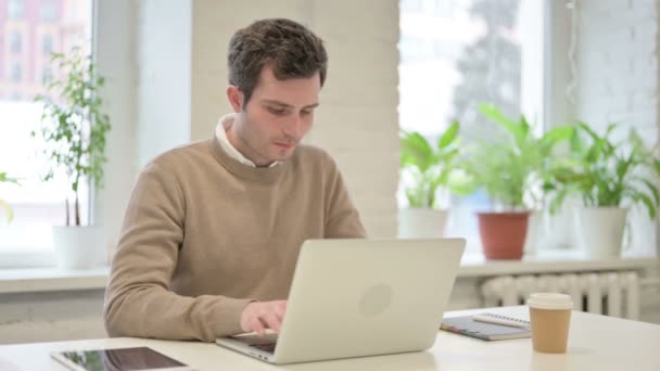 Чоловік усміхається в камері, користуючись ноутбуком у офісі — стокове відео