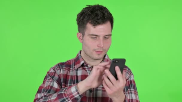 Портрет молодого человека, празднующего на смартфоне, зеленый хроматический экран — стоковое видео