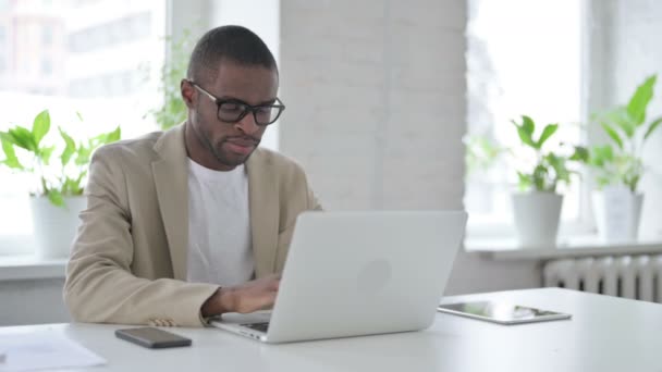 Homem africano mostrando polegares para baixo sinal ao usar laptop no escritório — Vídeo de Stock