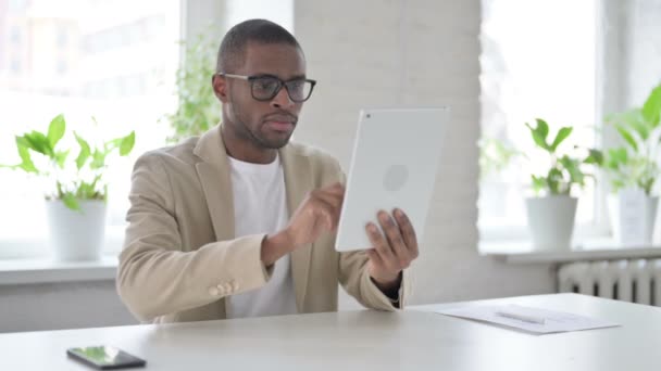 African Man świętuje sukces na tablecie w biurze — Wideo stockowe