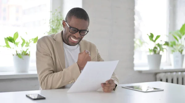 Afrikansk Man firar framgångar samtidigt läsa dokument i Office — Stockfoto