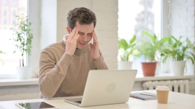 Dizüstü bilgisayarda çalışırken başı ağrıyan adam