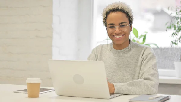 Afrikansk kvinna ler mot kameran när du använder laptop i Office — Stockfoto
