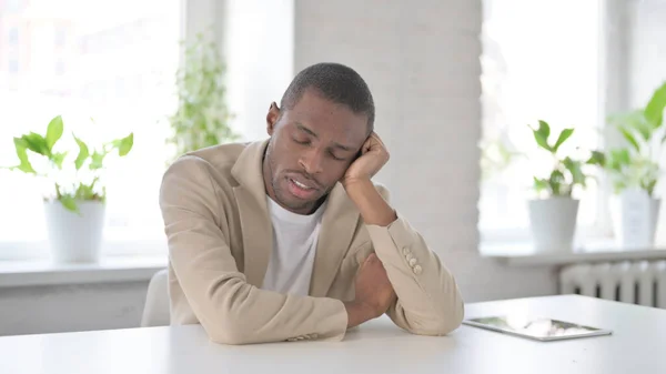 Sömnig afrikansk man som tar en tupplur när han sitter på kontoret — Stockfoto