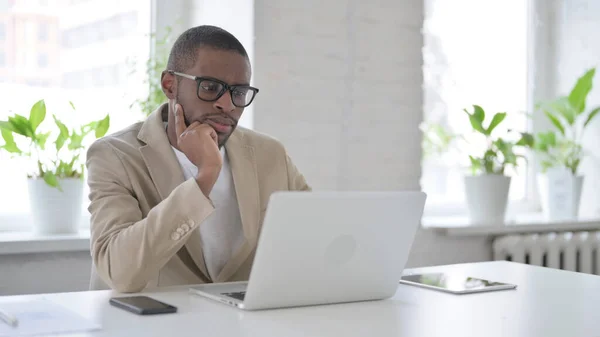 Hombre africano pensando mientras trabaja en el ordenador portátil en la oficina —  Fotos de Stock