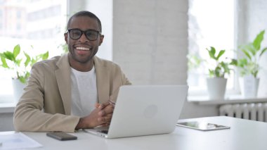 Ofiste dizüstü bilgisayar kullanırken kameraya gülümseyen Afrikalı Adam