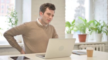 Ofiste dizüstü bilgisayar kullanırken sırt ağrısı çeken adam