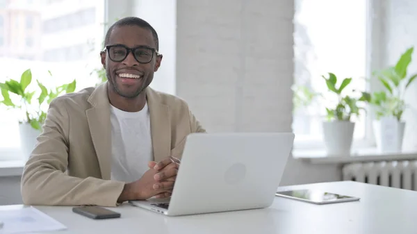 African Man Smiling at Camera while using Laptop in Office — Stockfoto