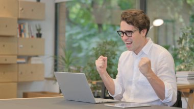 Genç Adam Modern Ofiste Dizüstü bilgisayar kullanırken Başarı Kutlaması