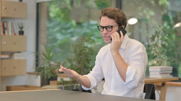 怒っている男は現代オフィスでスマートフォンで話している — ストック写真