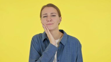 Dişi ağrıyan genç bir kadın, sarı arka planda dekolte.