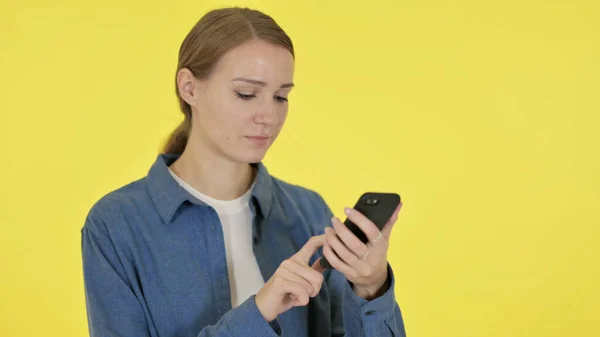 Молода жінка переглядає смартфон на жовтому тлі — стокове фото