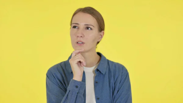 Junge Frau denkt über neuen Plan auf gelbem Hintergrund nach — Stockfoto