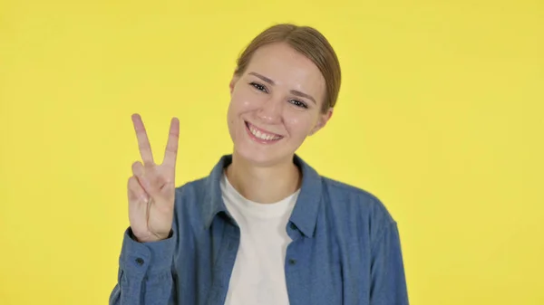 Mujer joven mostrando signo de victoria sobre fondo amarillo — Foto de Stock