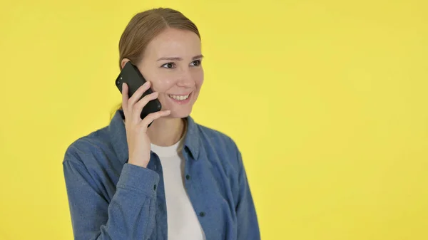 Giovane donna che parla al telefono su sfondo giallo — Foto Stock