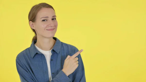 Mujer joven señalando hacia el producto sobre fondo amarillo — Foto de Stock