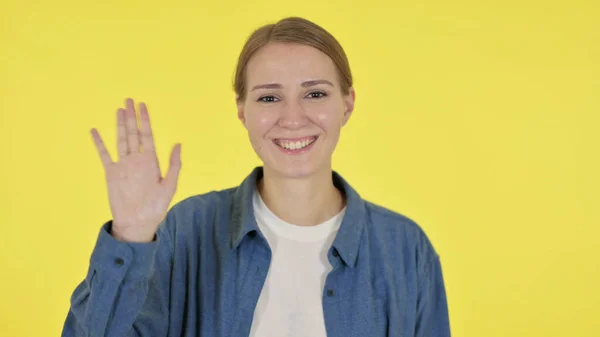 Jonge vrouw zwaaien, verwelkomen op gele achtergrond — Stockfoto