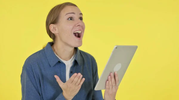 Mladá žena slaví úspěch na tabletu na žlutém pozadí — Stock fotografie
