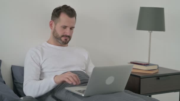 Férfi laptoppal mutatja hüvelykujját az ágyban — Stock videók