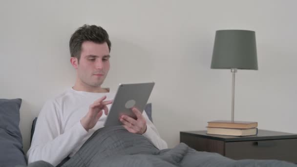 Homem comemorando o sucesso no tablet enquanto sentado na cama — Vídeo de Stock