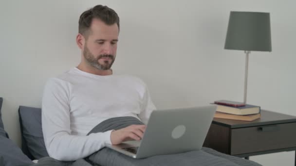 Mężczyzna z laptopem Patrząc na aparat w łóżku — Wideo stockowe