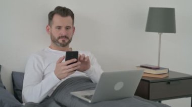 Kanepede akıllı telefon kullanan dizüstü bilgisayarlı bir adam. 