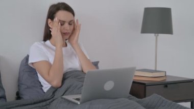 Yatakta dizüstü bilgisayarla uğraşırken kadın baş ağrısı çekiyor