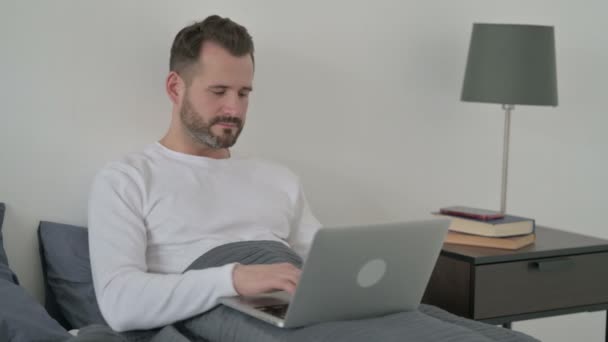 Hombre con el ordenador portátil diciendo No por la cabeza agitar en la cama — Vídeos de Stock