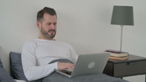 Mann mit Rückenschmerzen arbeitet im Bett am Laptop — Stockvideo