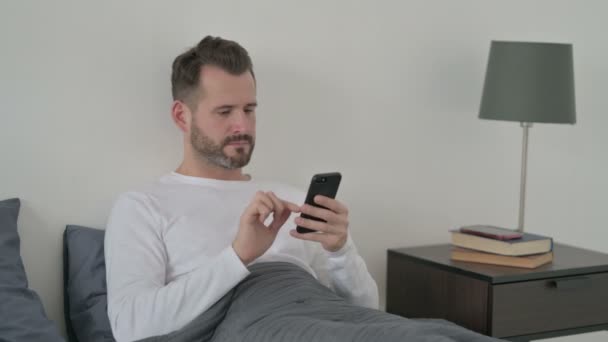Mann som bruker smarttelefon i senga – stockvideo