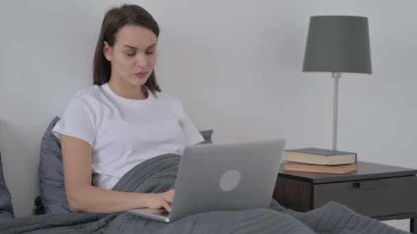 Женщина празднует успех на ноутбуке в постели — стоковое видео
