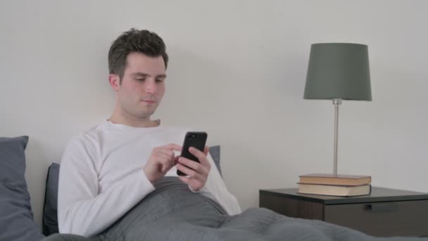 Man viert succes op Smartphone in bed — Stockvideo
