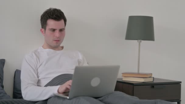 Hombre reaccionando a la pérdida en el ordenador portátil en la cama — Vídeos de Stock