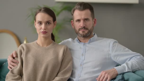 Portret pary patrzącej w kamerę siedzącej na kanapie — Wideo stockowe
