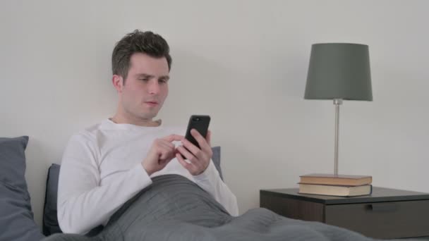 Mann reagiert auf Verlust mit Smartphone im Bett — Stockvideo