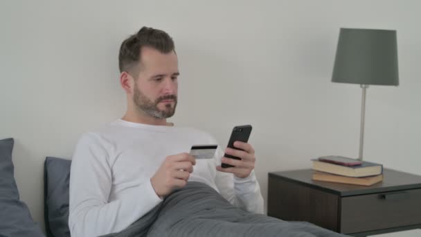 Hombre haciendo el pago en línea en el teléfono inteligente en la cama — Vídeo de stock