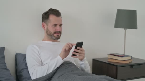 Mann reagiert auf Verlust mit Smartphone im Bett — Stockvideo