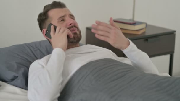 Wütender Mann spricht im Bett auf Smartphone — Stockvideo