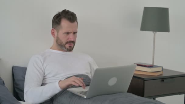 Homem reagindo à perda no portátil na cama — Vídeo de Stock